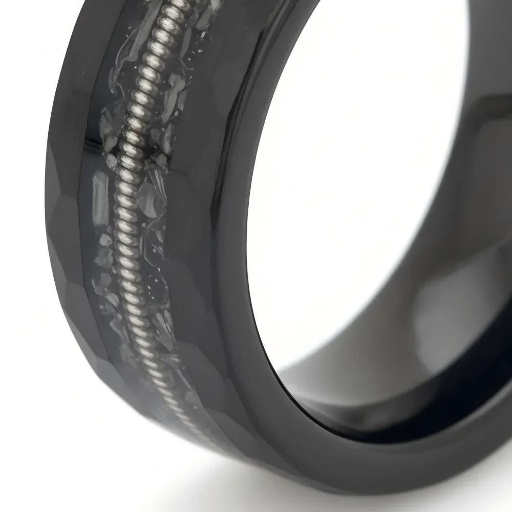 Macro detail of geometric faceted edges and intricate coiled metallic wire on The Resonance showcasing polished Obsidian and a guitar string.