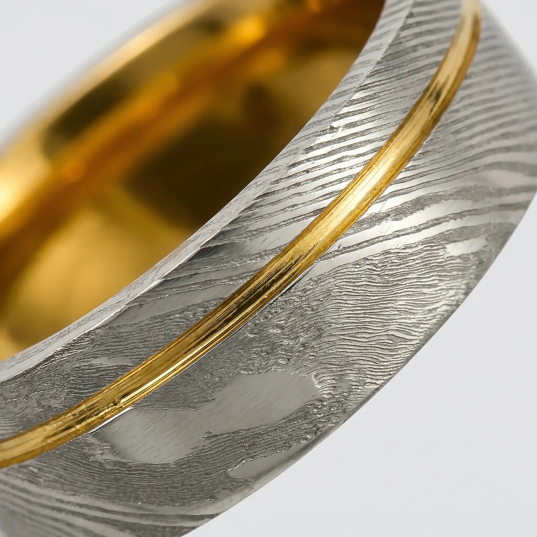 Macro detail of Stratigraphic acid-etching pattern and precision-milled gold groove on The Meridian Fold showcasing Forged Damascus Steel and 18K Gold PVD coating.