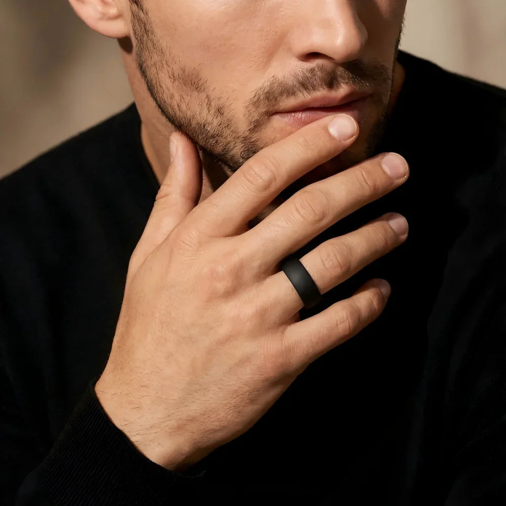 Man's hand wearing The Shadow Monolith black sandblasted ring, raised with fingers resting lightly near the chin in a focused, contemplative pose.