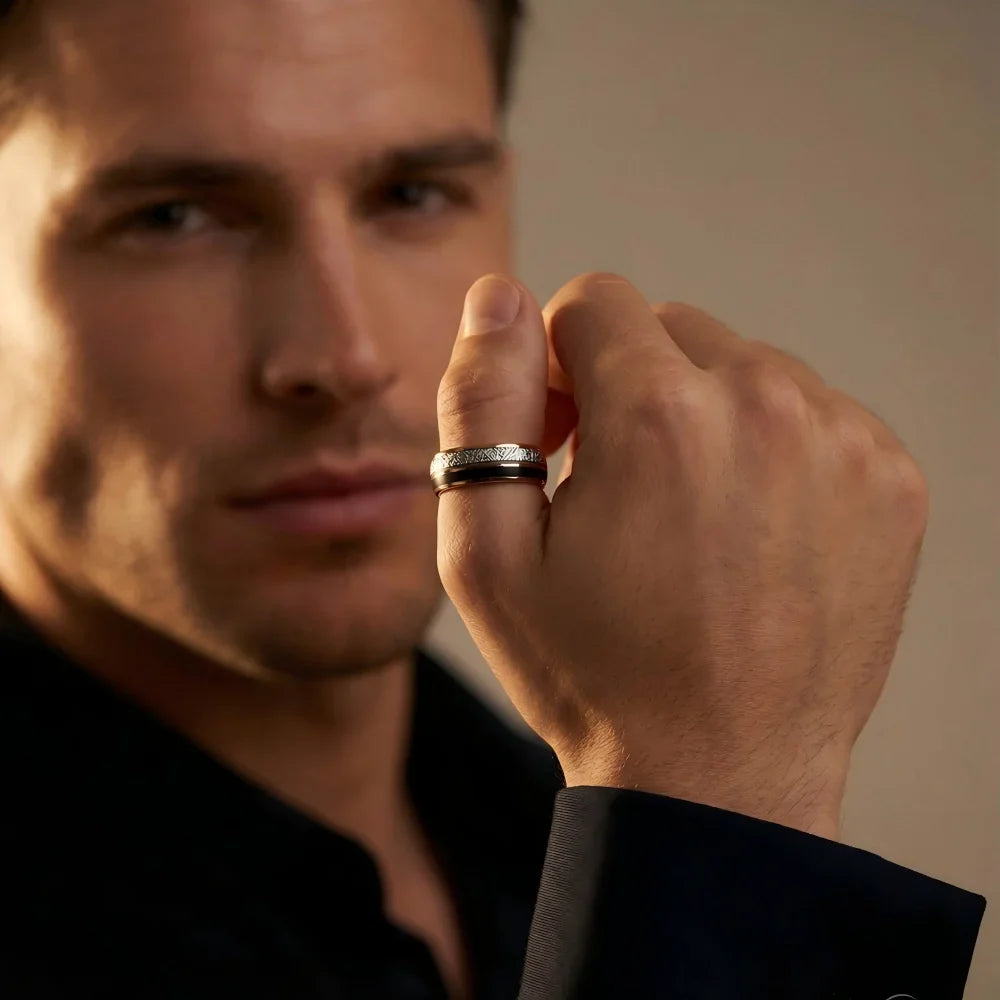 Man's hand wearing The Stellar Path 18K Rose Gold PVD and Meteorite ring, raised in a precise geometric gesture under warm, dramatic studio lighting.