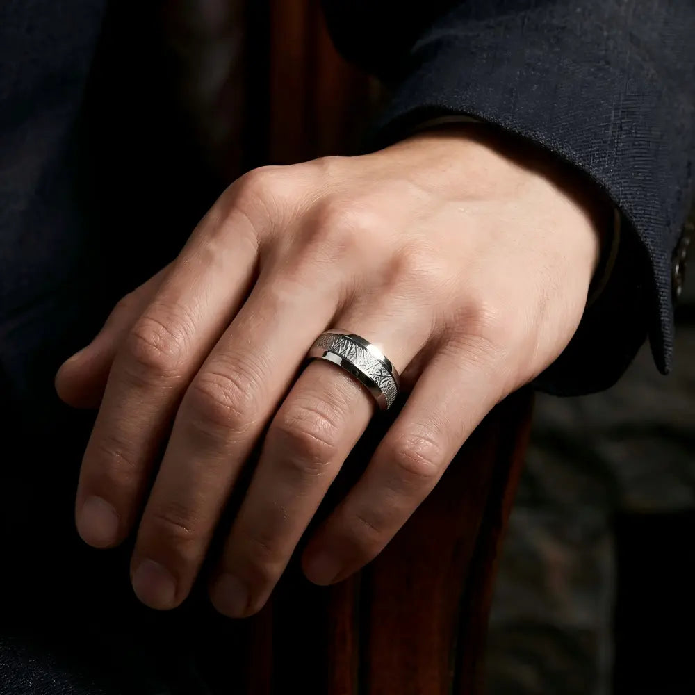 Man's hand wearing The Astral Pathway Aerospace-grade Tungsten ring resting on a dark tailored suit cuff in a focused professional setting.