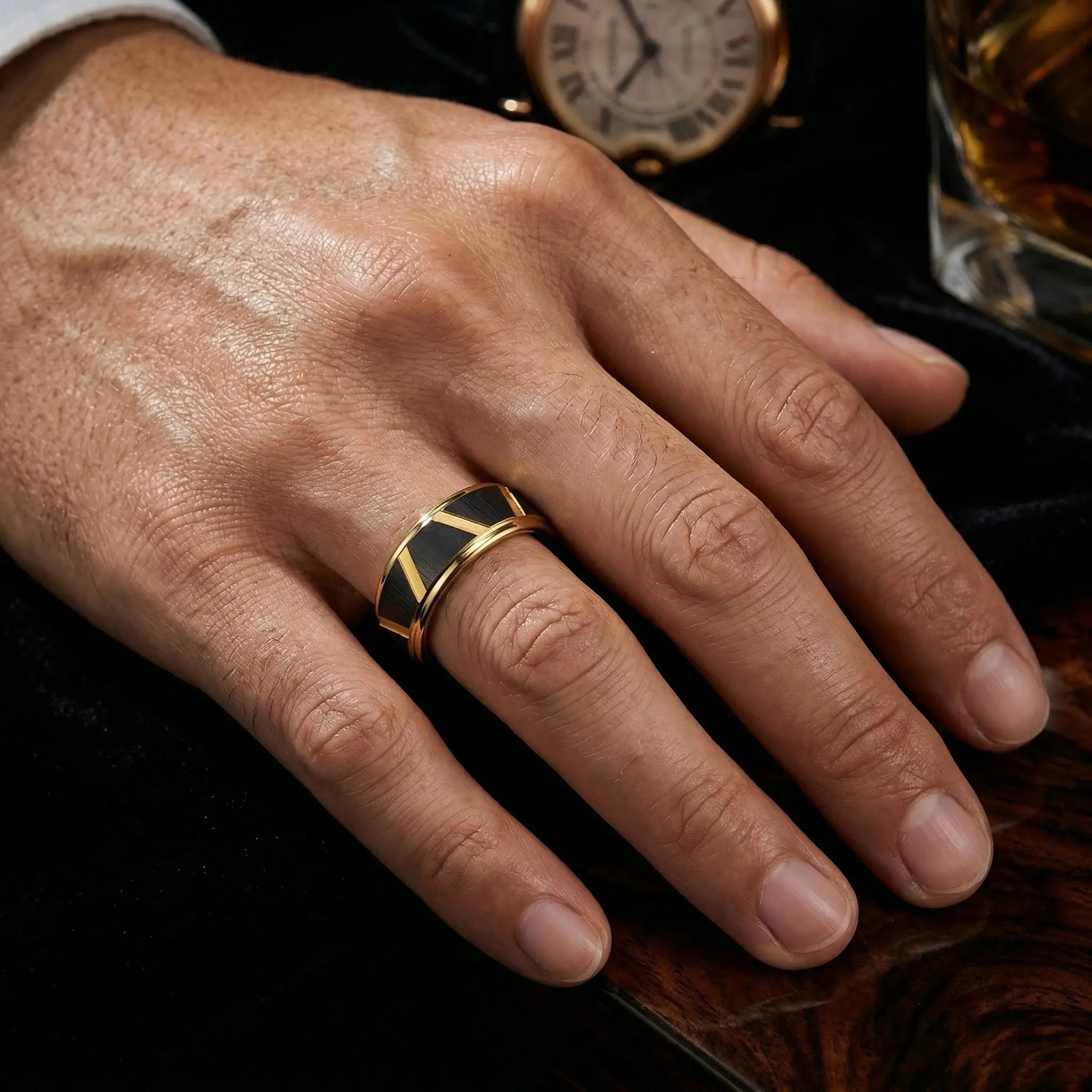 Man's hand wearing The Linear Divide Aerospace-grade Tungsten ring resting on a dark structured wooden surface with a classic timepiece in the background.