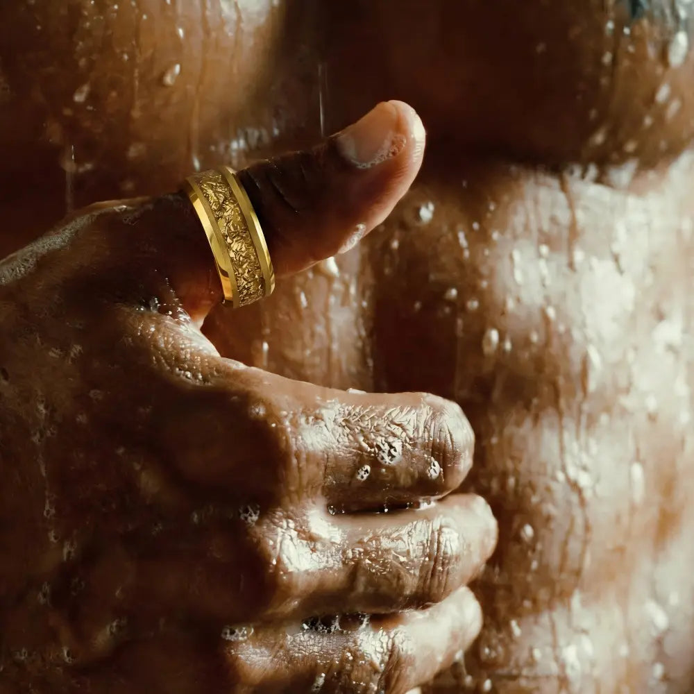 Textured gold tungsten ring on thumb of wet hand, closeup jewelry detail, water droplets visible