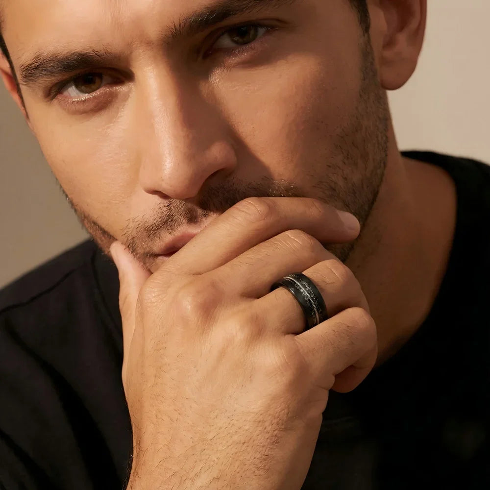 Man's hand wearing The Resonance faceted Obsidian ring, raised with fingers resting lightly against the jawline in a focused studio setting.