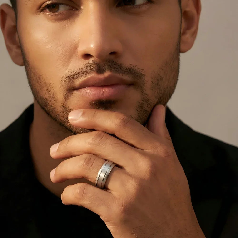 Man's hand wearing The Argent Monolith silver-tone Aerospace-grade Tungsten ring, raised with fingers lightly touching the chin in a focused, contemplative pose.