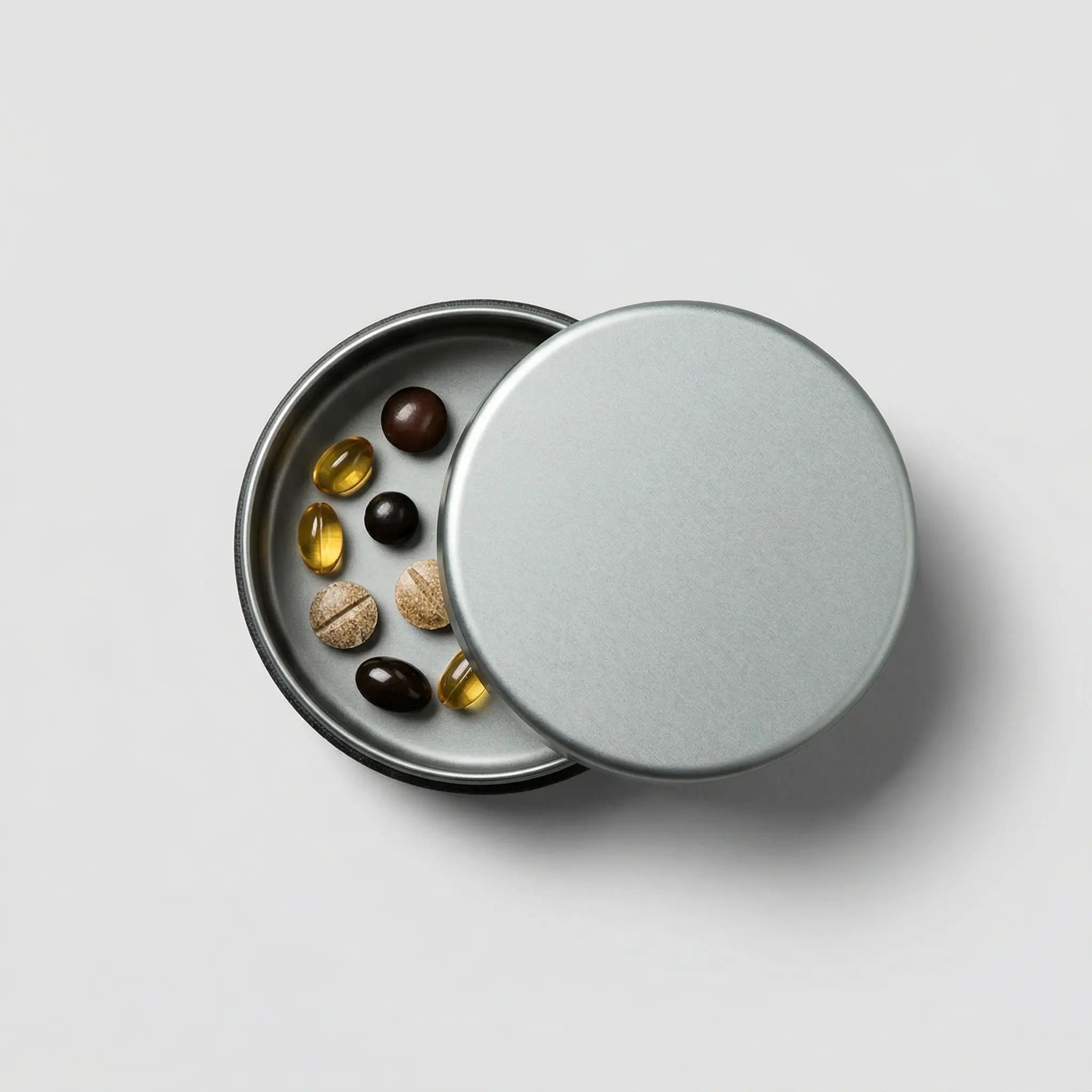 Modern round metal container with assorted capsules and tablets on a light surface