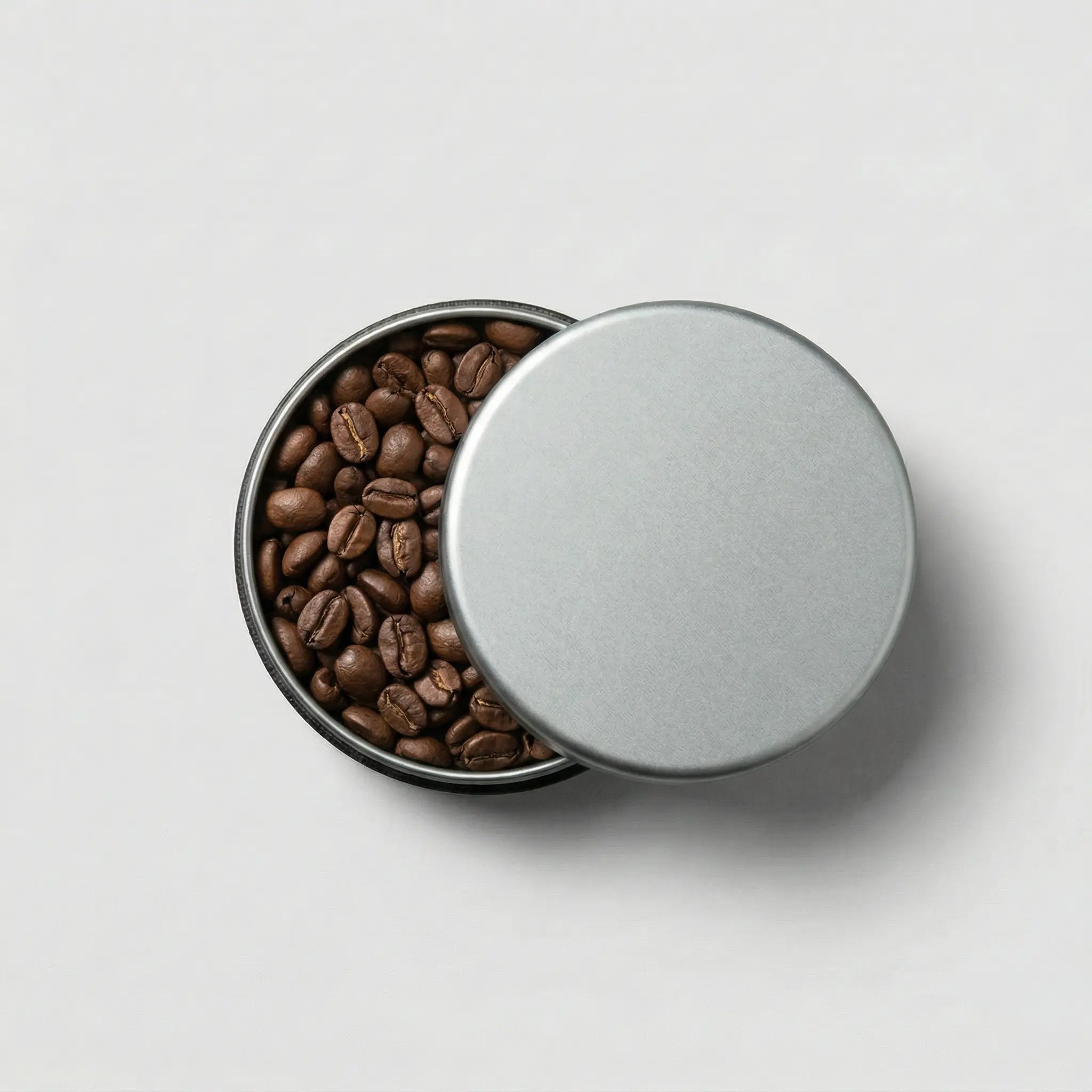 Round tin container filled with roasted coffee beans on a white background