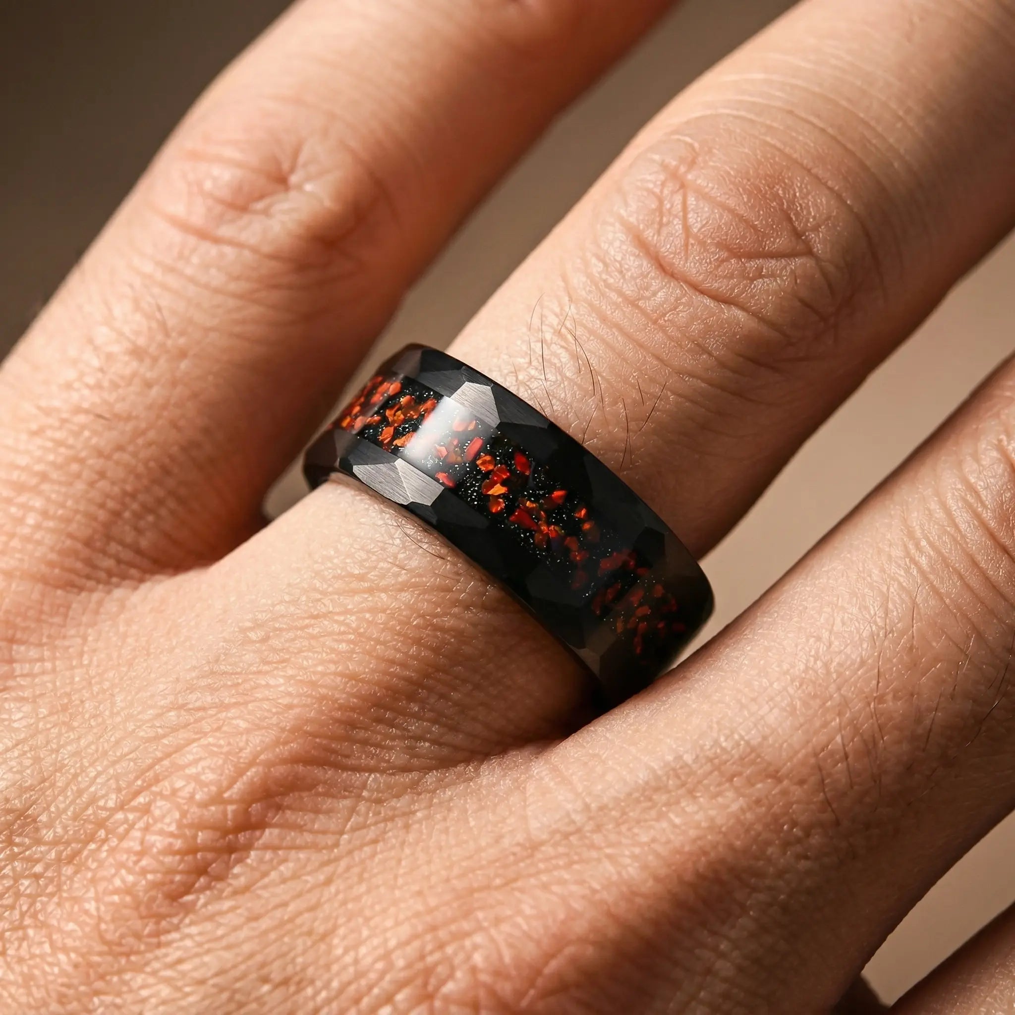 Man's hand wearing The Ignis Forge Black Aerospace-grade Tungsten ring resting naturally under warm dramatic studio lighting.