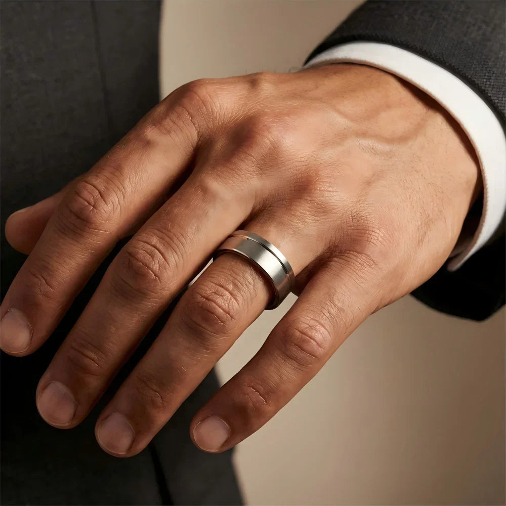 Man's hand wearing The Heritage Cask Aerospace-grade Tungsten ring extended slightly against a dark tailored wool suit sleeve in a refined environment.