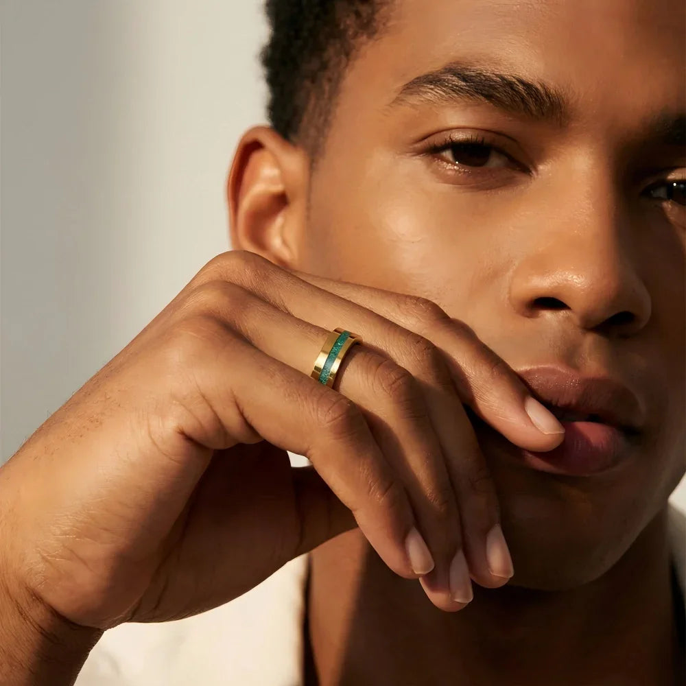 Man's hand wearing The Verdant Monolith 18K Gold PVD Tungsten ring resting naturally near the face in a focused, structured portrait setting.