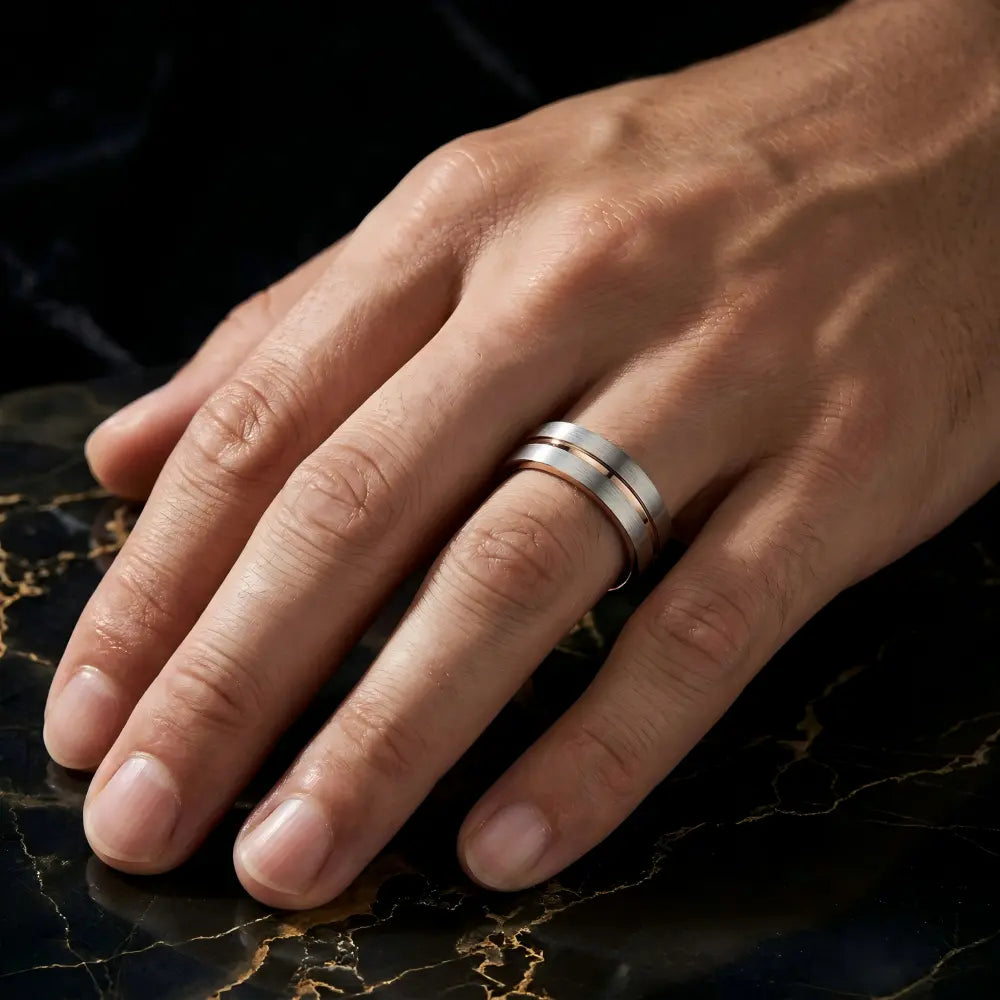 Man's hand wearing The Rose Meridian Aerospace-grade Tungsten ring resting flat on a dark structured marble surface with gold veins.