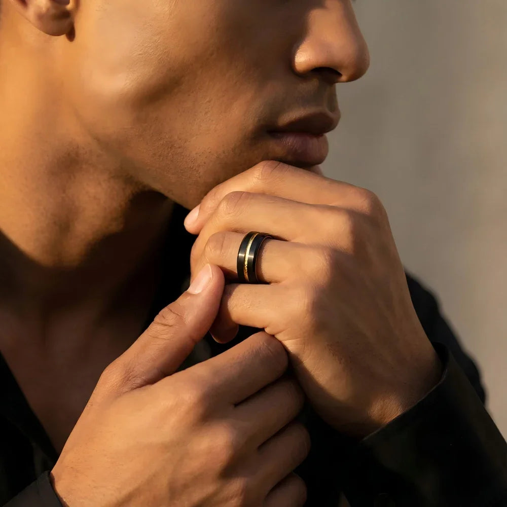 Man's hand wearing The Aurelius Spark Black Aerospace-grade Tungsten ring resting thoughtfully against the jawline in a focused architectural studio setting.